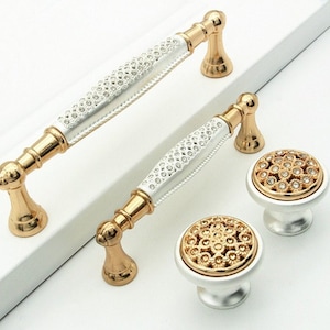 Può includere: Due pomelli per armadietti argentati e dorati con un motivo a diamante e due tiretti abbinati con un motivo a diamante.