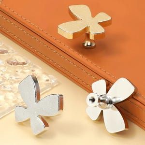 Op de afbeelding: Drie decoratieve kastknoppen in de vorm van een bloem. Eén knop is goud, de andere twee zijn zilver.