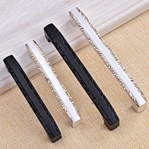 May include: Four cabinet pulls with an ornate design. Two are silver with gold accents and two are black.