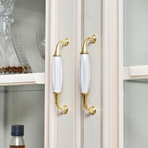 May include: Two white ceramic cabinet knobs with gold accents. The knobs have a decorative, fluted design.