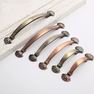 May include: Six antique-style cabinet pulls with a shell design. The pulls are made of metal and have a variety of finishes, including copper, bronze, and brass.