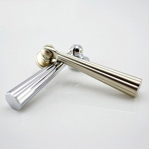 May include: Two cabinet pulls, one silver and one gold, with a fluted design. The pulls are made of metal and have a rounded end.