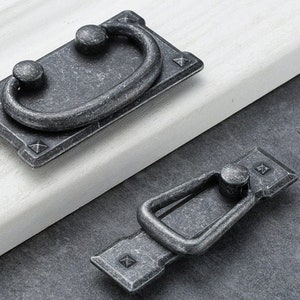 Puede incluir: Dos tiradores de cajón de plata antigua con un diseño de anillo. Los tiradores tienen un acabado desgastado y están hechos de metal.