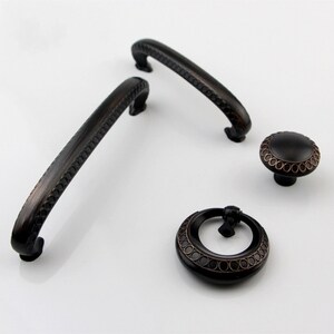 Peut inclure: Ensemble de trois boutons de cabinet noirs avec un design orné. Les boutons ont une forme circulaire avec un bord surélevé et un motif de petits cercles autour du bord. Les boutons sont en métal et ont une finition brossée.