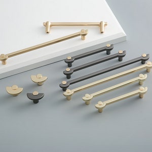 May include: A set of 10 modern cabinet hardware pulls in gold and black finishes. The pulls feature a simple, geometric design with rounded edges. The pulls are available in two sizes.