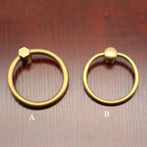 Könnte beinhalten: Zwei Messing-Schranktürgriffe. Der Griff links hat einen sechseckigen Knopf. Der Griff rechts hat einen runden Knopf.