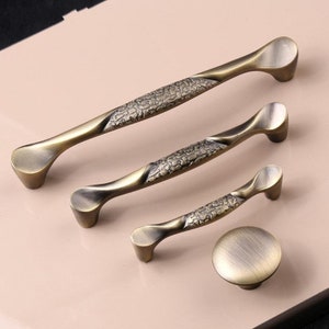 Könnte beinhalten: Satz von drei antiken goldenen Schrankknöpfen mit strukturiertem Design. Die Knöpfe sind in verschiedenen Größen und haben eine abgerundete Form. Es gibt auch einen passenden einzelnen Knopf.