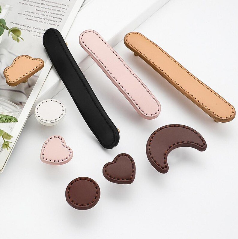 May include: Assortment of leather drawer pulls in various shapes and colours, including pink, brown, and black. The pulls feature a stitched design and are perfect for adding a touch of style to any drawer.