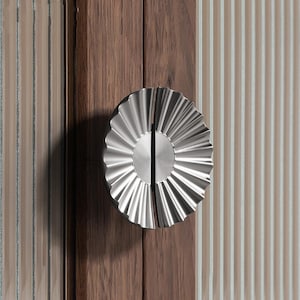 Könnte beinhalten: Ein silberfarbener, dekorativer Türgriff mit einem gewellten Design. Der Griff ist in zwei Hälften geteilt und hat eine kreisförmige Mitte.