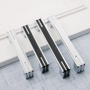 May include: Four silver cabinet pulls with black accents. The pulls have a rectangular shape with a groove down the center.