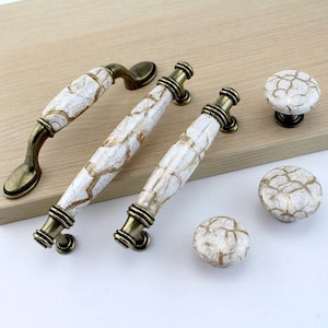 May include: Set of five antique gold cabinet knobs with white ceramic bases featuring a crackled gold design.