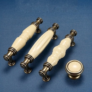 May include: Three antique brass cabinet knobs with off-white ceramic handles. The handles have a textured, speckled finish.