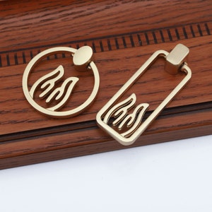 May include: Two gold-toned metal cabinet pulls with a flame design. One pull is round and the other is rectangular.