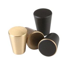 May include: Four cabinet knobs in different finishes: gold, brass, and black. The knobs are cone-shaped with a rounded top.