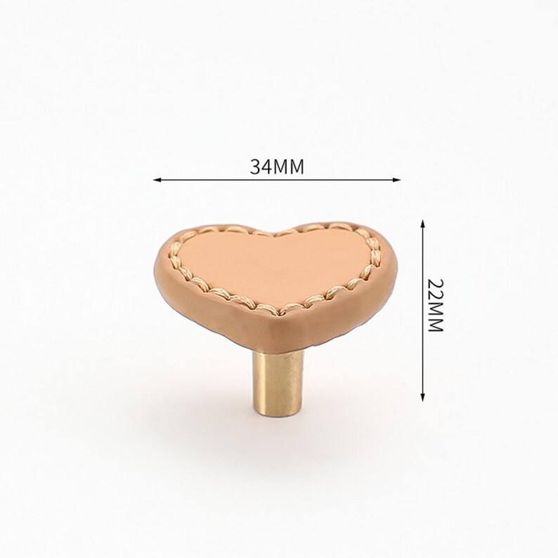 May include: A heart-shaped cabinet knob with a light brown leather surface and gold stitching. The knob measures 34mm wide and 22mm high.