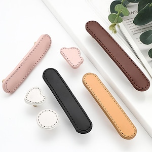 May include: Assortment of six leather drawer pulls in various shapes and colours, including pink, brown, black, and beige. The pulls have a stitched design and are suitable for cabinets, drawers, and furniture.