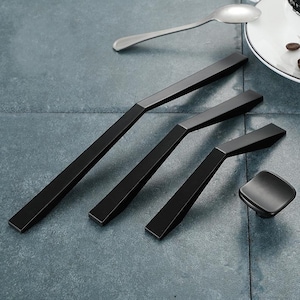May include: Four black metal cabinet pulls with a geometric design. The pulls are arranged in a row from largest to smallest. The smallest pull is a square knob.