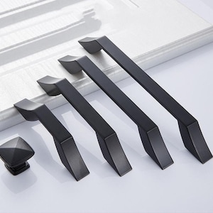 Puede incluir: Cuatro tiradores de armario de metal negro con un diseño moderno y angular. Los tiradores están dispuestos en una fila, con el tirador más grande en la parte superior y el más pequeño en la parte inferior. Los tiradores están hechos del mismo material y tienen un acabado liso y pulido.