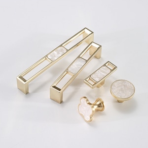 Puede incluir: Conjunto de cinco pomos y tiradores de armario dorados con incrustaciones de nácar blanco. Los pomos y tiradores tienen un diseño geométrico.