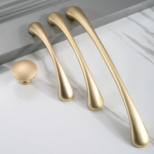 May include: Four gold-toned cabinet pulls with a teardrop shape. The pulls are arranged in a row from largest to smallest. A smaller gold-toned knob is also included.