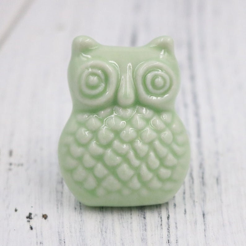 May include: A light green ceramic owl figurine with a detailed textured body and large, round eyes.