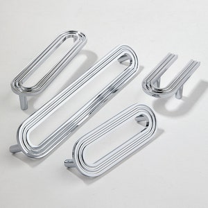 May include: Set of four chrome cabinet pulls with a modern, geometric design. The pulls are oval-shaped with multiple concentric rings. One pull is a smaller U-shape.