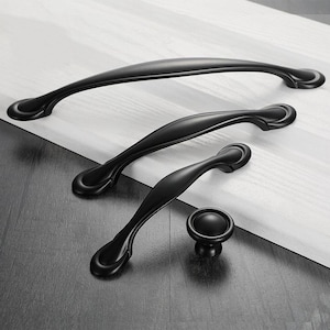 Puede incluir: Cuatro tiradores de armario negros con un diseño simple y elegante. Los tiradores son de diferentes tamaños, siendo el más grande de unos 25 cm de largo. El tirador más pequeño es un pomo.