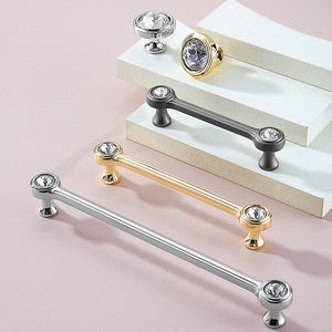 Può includere: Quattro pomelli e maniglie per armadi con dettagli in cristallo. I pomelli sono rotondi e le maniglie sono lunghe e dritte. I pomelli e le maniglie sono disponibili in argento, oro e nero.