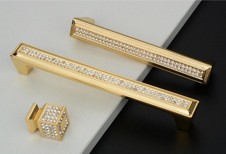 May include: Two gold cabinet pulls with a row of clear rhinestones and a smaller gold knob with clear rhinestones.