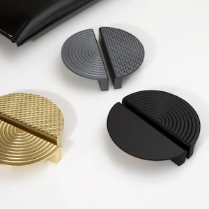 May include: Four half-circle cabinet pulls in different finishes. The pulls are made of metal and have a textured design. The finishes are gold, black, gray, and a darker gray.