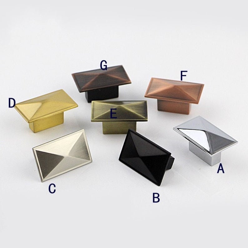 Puede incluir: Surtido de ocho pomos de armario en varios acabados, incluyendo negro, plata, oro y cobre. Los pomos son rectangulares con una parte superior en forma de pir&aacute;mide.