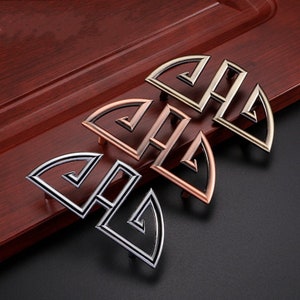 Könnte beinhalten: Drei dekorative Schranktürgriffe in Silber, Kupfer und Gold. Jeder Griff hat ein geometrisches Design mit einer Halbkreisform.