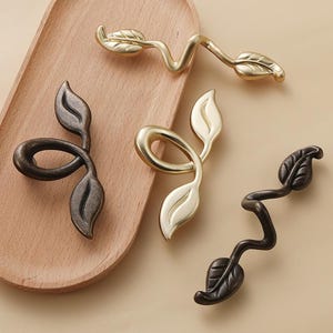May include: Four decorative cabinet pulls with a leaf design. Two are gold and two are black.