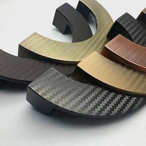 May include: A set of five cabinet pulls in different finishes, including black, bronze, copper, and gold. The pulls have a curved shape and a textured surface.