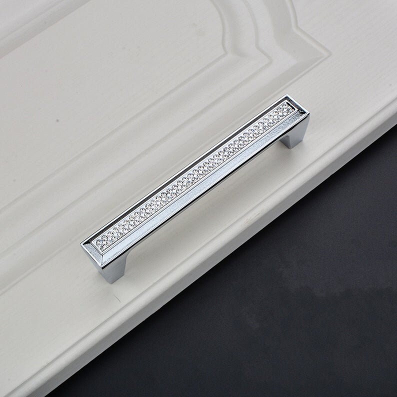 May include: A silver cabinet door handle with a row of clear rhinestones.