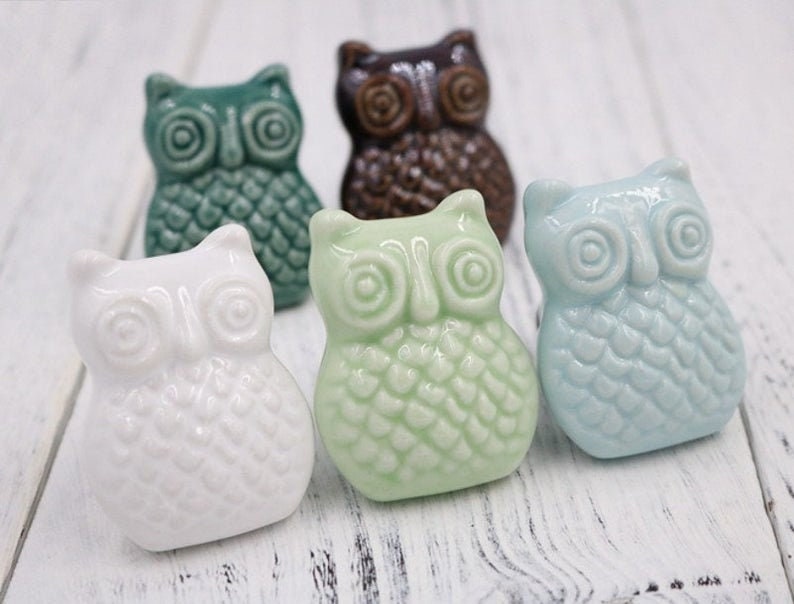 May include: Five ceramic owl drawer pulls in different colours: white, green, blue, brown, and teal. Each owl has a detailed design with raised eyes and feathers.