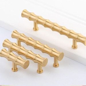 Op de afbeelding: Vier gouden bamboe-stijl kastgrepen in verschillende maten. De grepen hebben een eenvoudig, modern ontwerp.