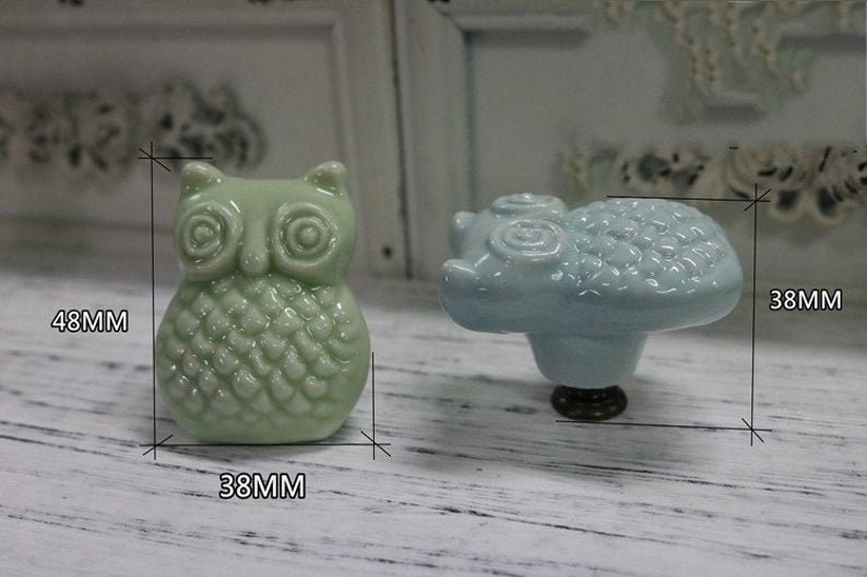 May include: Two ceramic drawer pulls, one shaped like an owl and one shaped like a cloud. The owl is green and the cloud is light blue. Both are 38 mm wide and the owl is 48 mm tall.