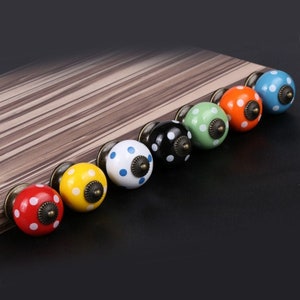 May include: Seven ceramic cabinet knobs with a polka dot pattern in various colors, including red, yellow, blue, green, and black. Each knob has a small, round, antique brass accent.