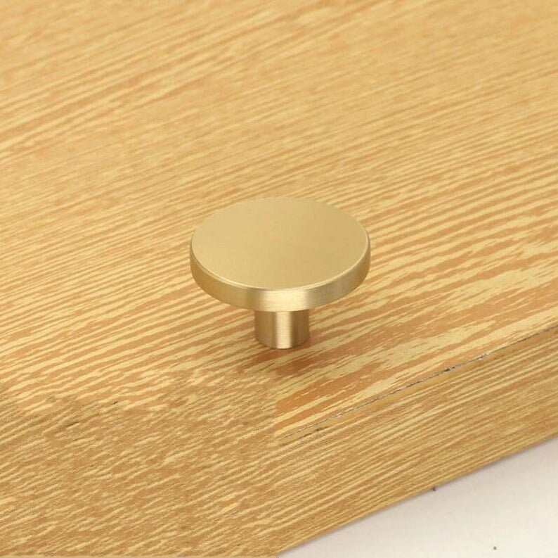 May include: A round, gold-toned cabinet knob with a smooth, flat surface and a cylindrical base.