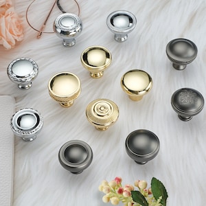 Pode incluir: Conjunto de botões decorativos para armários em vários acabamentos, incluindo prata, ouro e preto. Os botões têm diferentes designs, incluindo redondo, quadrado e ornamentado.