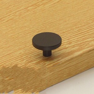 May include: Black round cabinet knob with a flat top and a cylindrical base.