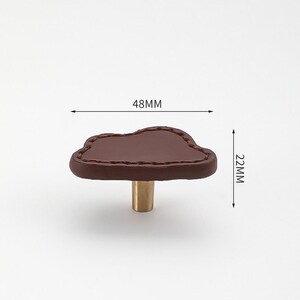 May include: Brown leather cloud-shaped cabinet knob with a brass base. The knob measures 48mm wide and 22mm high.