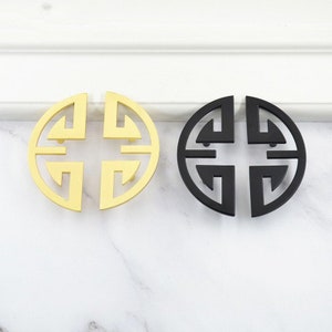 以下が含まれることがあります： 幾何学模様の丸いキャビネットノブが2つ。1つは金色、もう1つは黒色です。