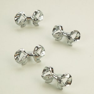 Puede incluir: Cuatro tiradores de cajón en forma de lazo de color plateado. Los tiradores son de metal y tienen un acabado brillante.