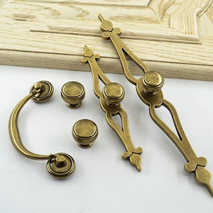 May include: Set of four antique brass cabinet knobs and a pull. The knobs are round with a decorative design. The pull is curved with a decorative design.