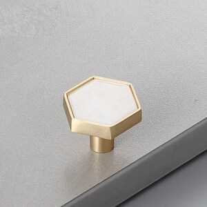 Pu&ograve; includere: Un pomello per armadio esagonale con un centro in ceramica bianca e una cornice in metallo dorato.