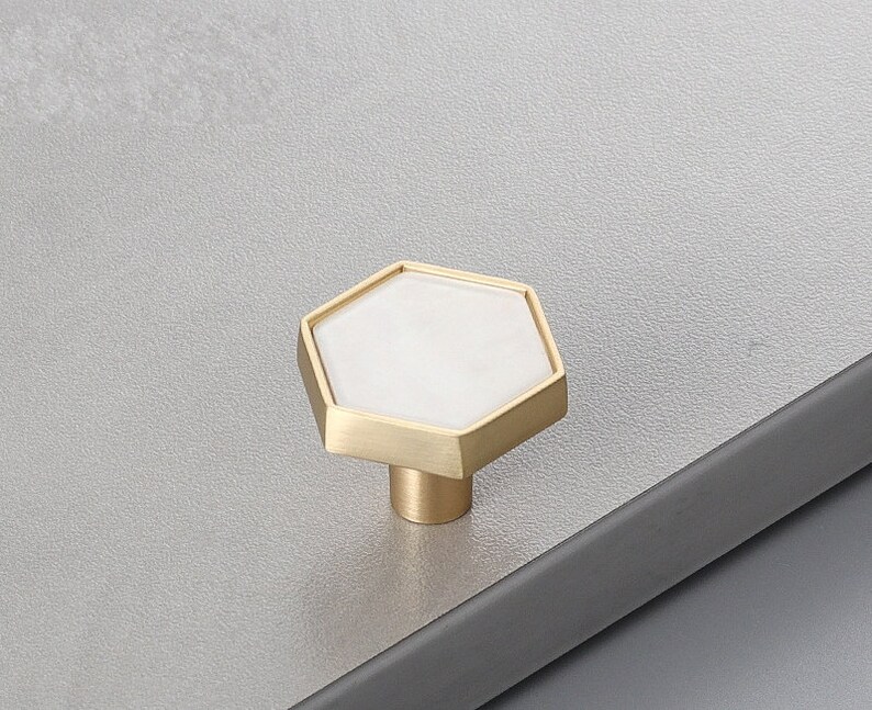 Pu&ograve; includere: Un pomello per armadio esagonale con un centro in ceramica bianca e una cornice in metallo dorato.