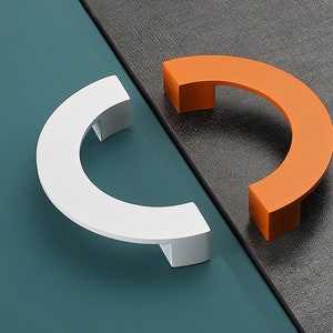 Peut inclure: Deux poignées de tiroir en demi-cercle, l'une blanche et l'autre orange. Les poignées sont en métal et ont une finition lisse et arrondie.
