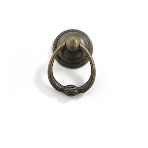 May include: Antique brass ring pull cabinet door handle with a decorative design.